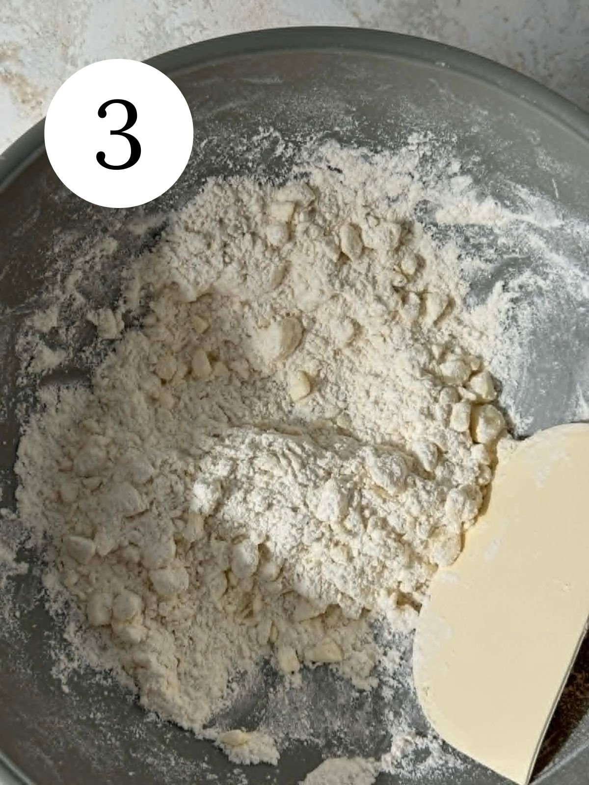 Butter cut into flour in a bowl with a bench scraper.