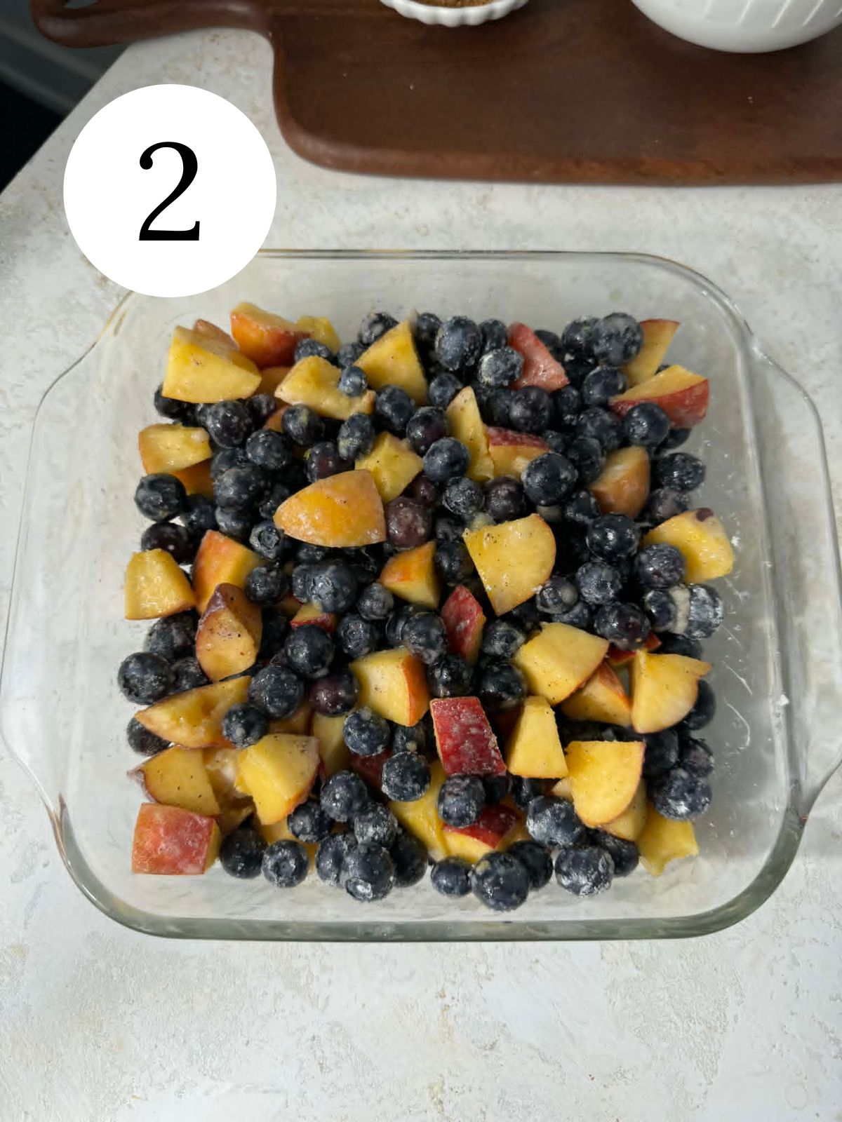 A glass baking dish filled with blueberries and peaches.