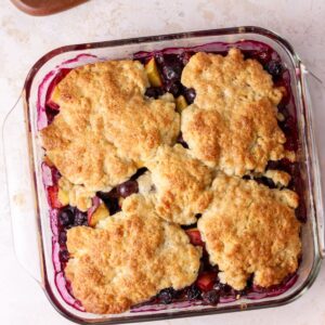 Peach and blueberry cobbler in a square glass baking dish.