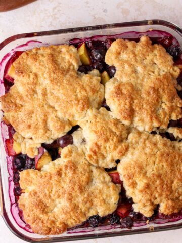 Peach and blueberry cobbler in a square glass baking dish.