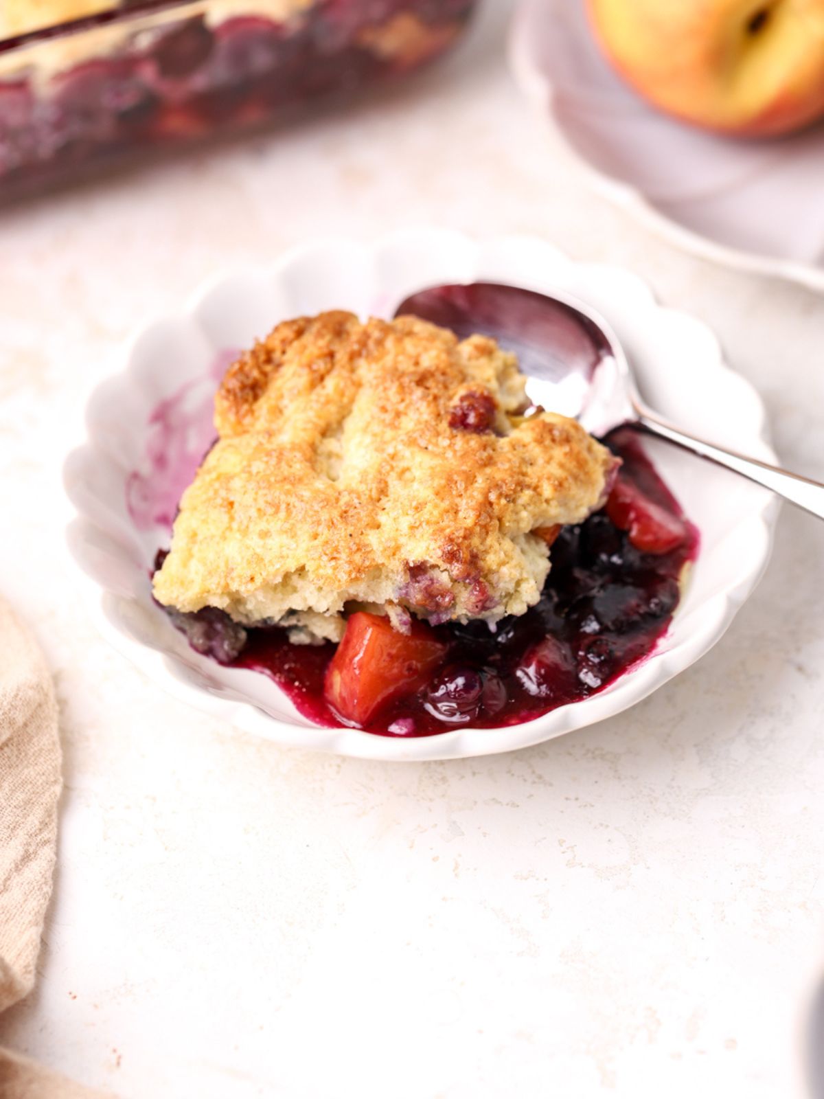 A bowl with blueberry peach cobbler and a spoon. 