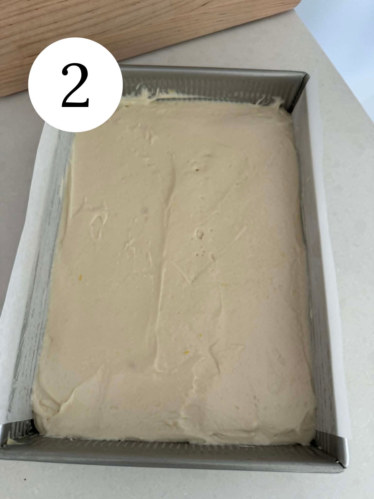 Cake batter spread in a rectangular pan lined with parchment paper.