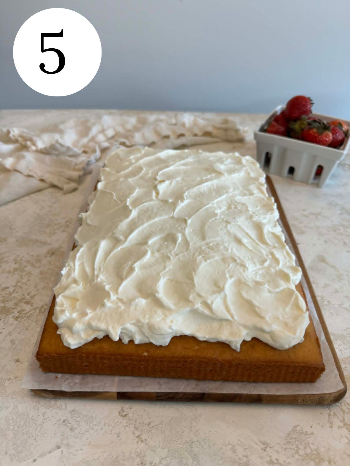 A sheet cake with whipped cream next to a bowl of berries.