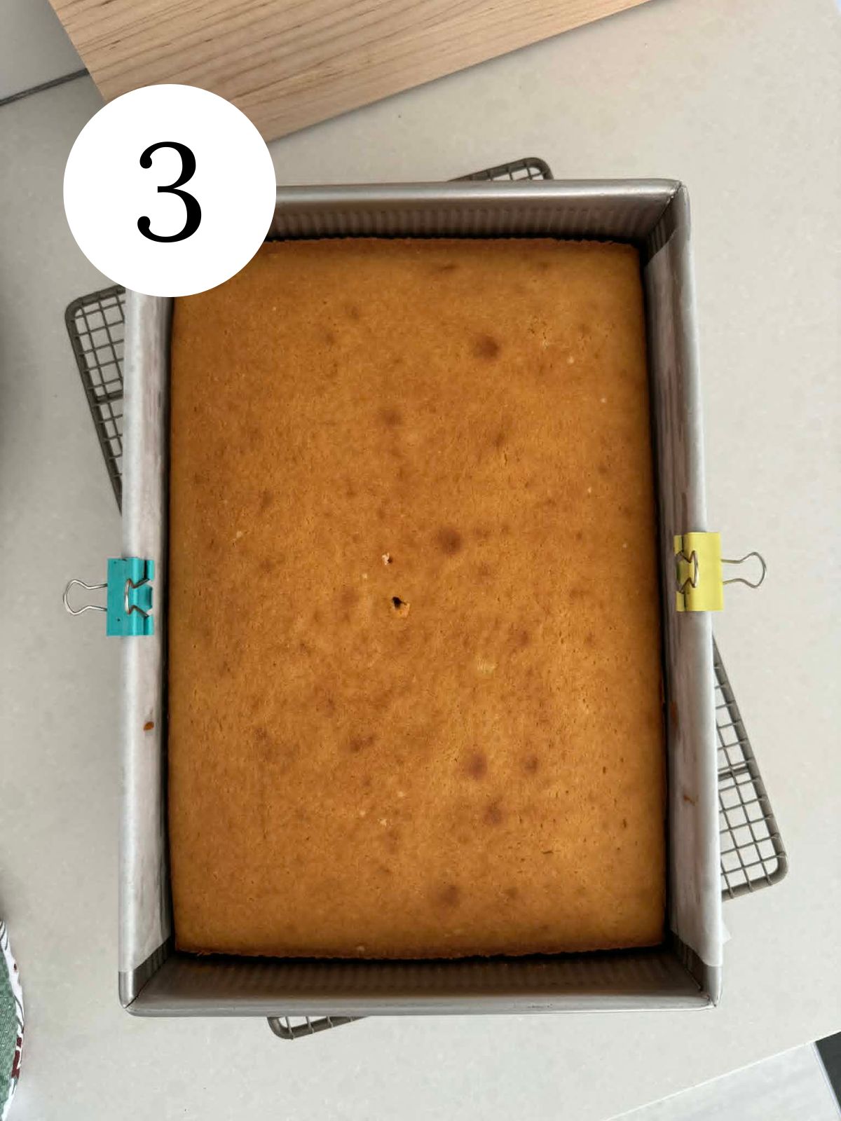 A golden cake in a rectangular pan on a wire rack.