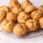A batch of golden brown choux puffs on a round wire rack.