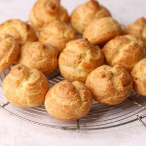 A batch of golden brown choux puffs on a round wire rack.