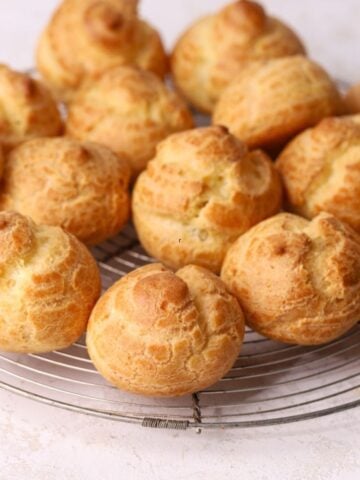 A batch of golden brown choux puffs on a round wire rack.