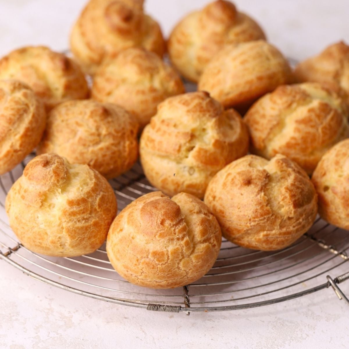 A batch of golden brown choux puffs on a round wire rack.