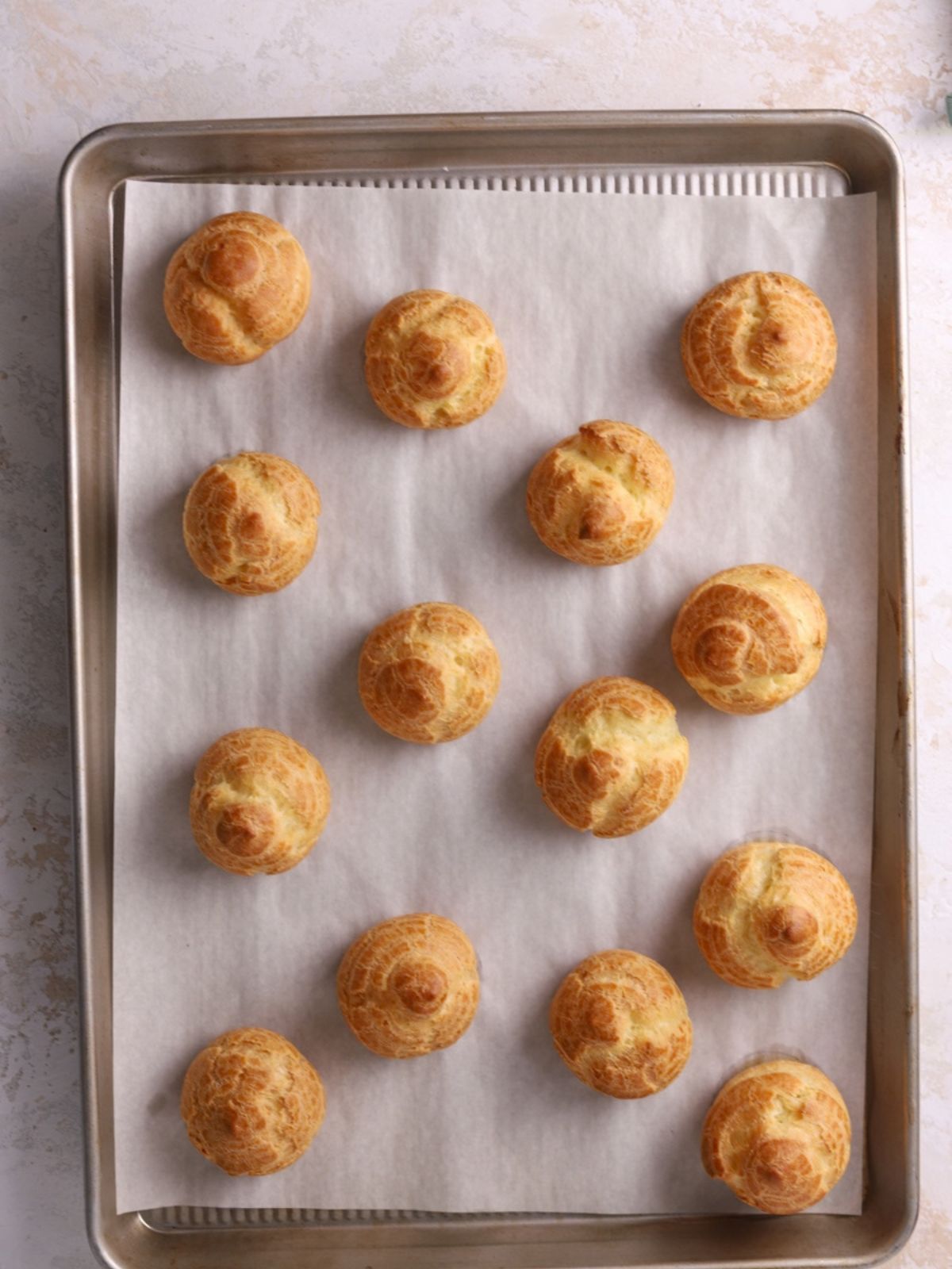 Cream puffs on a baking sheet lined with parchment paper.